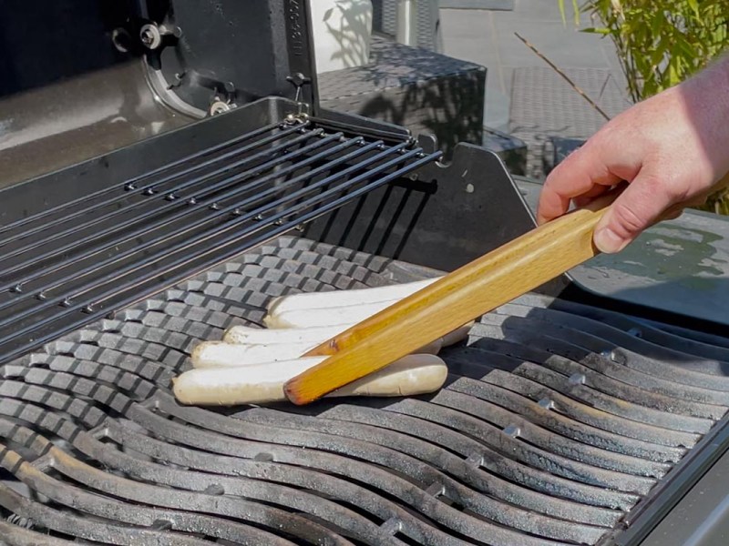Bratwürste werden auf einen Gasgrill gelegt.